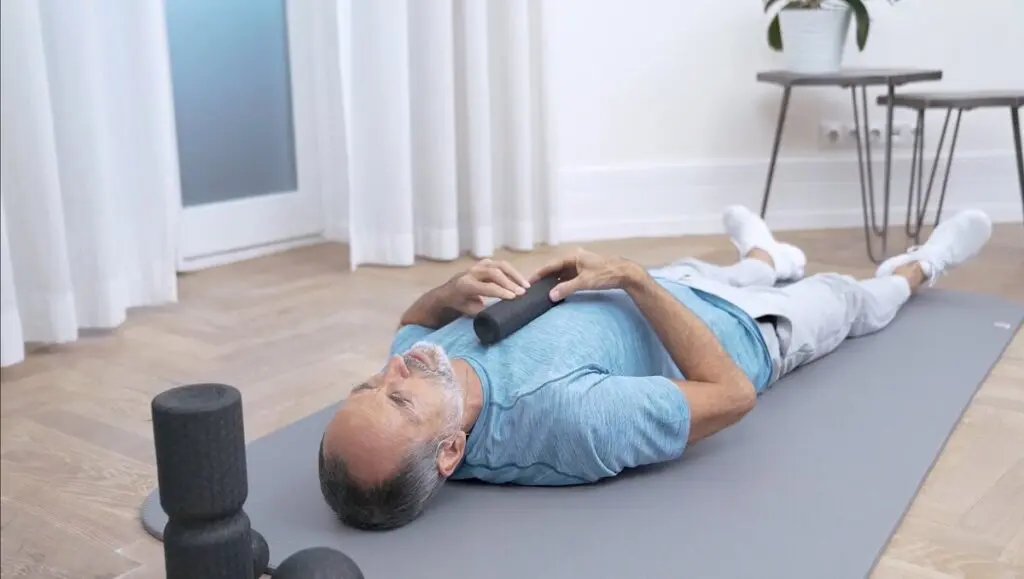 Ein Mann liegt auf einer Übungsmatte und legt eine Faszienrolle auf seine Brust, um eine Faszien-Rollmassage gegen Schulterschmerzen durchzuführen