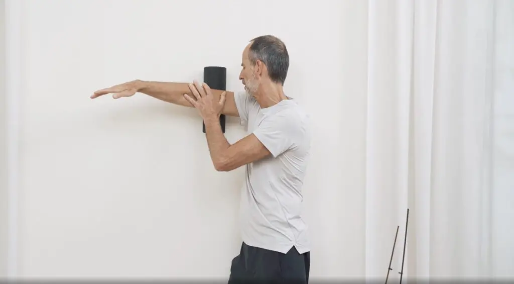 Ein Mann drückt mit seinem Trizeps eine Faszienrolle gegen die Wand