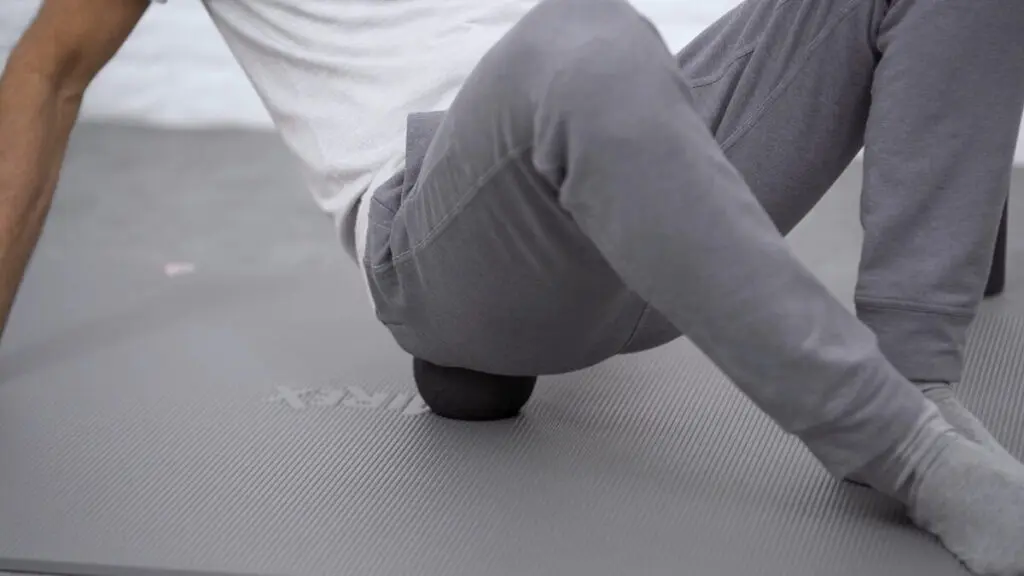 Nahaufnahme einer Faszienkugel, auf der ein Mann sitzt, um eine Faszien-Rollmassage am Gesäß durchzuführen