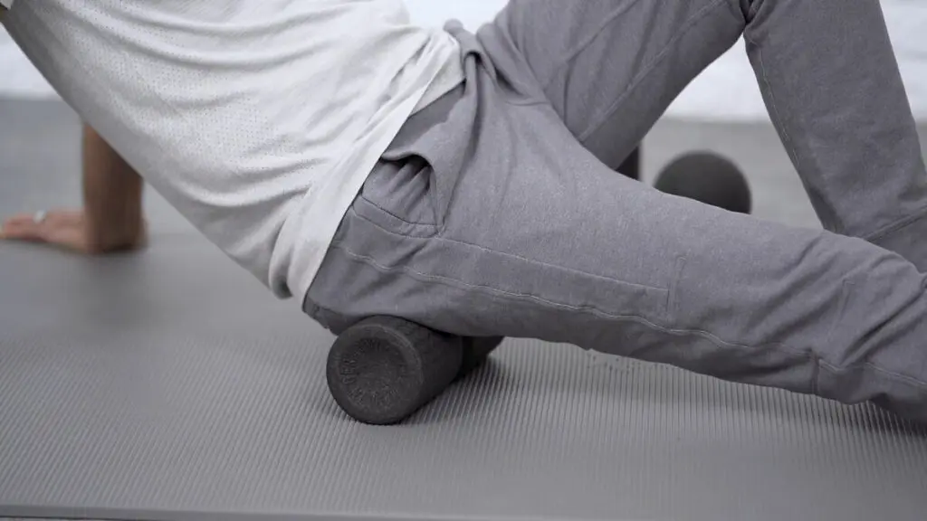 Zu sehen ist ein Mann, der mit dem Gesäß auf einer mittelgroßen Faszienrolle sitzt und sich nach hinten mit den Händen abstüzt.