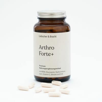 Zu sehen ist eine Braunglasflasche des Nahrungsergänzungsmittels Arthro Forte+. Die Flasche ist geöffnet, der Deckel lehnt an der Flasche und einige Nahrungsergänzungsmittel liegen vor der Flasche.
