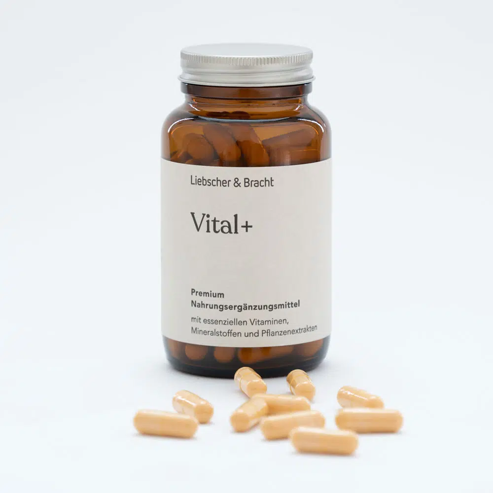 Zu sehen ist eine Braunglasflasche des Nahrungsergänzungsmittels Vital+. Die Flasche ist geöffnet, der Deckel lehnt an der Flasche und einige Nahrungsergänzungsmittel liegen vor der Flasche.