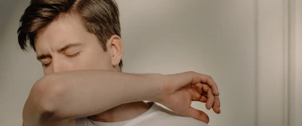 Ein Mann hustet in die Armbeuge.