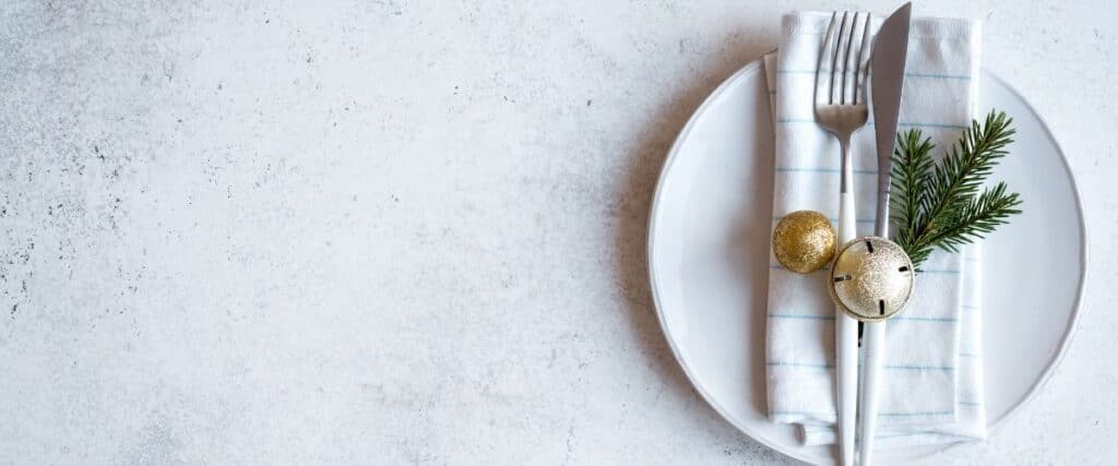 Auf einem Teller liegt Besteck, eine Serviette und ein Tannenzweig.