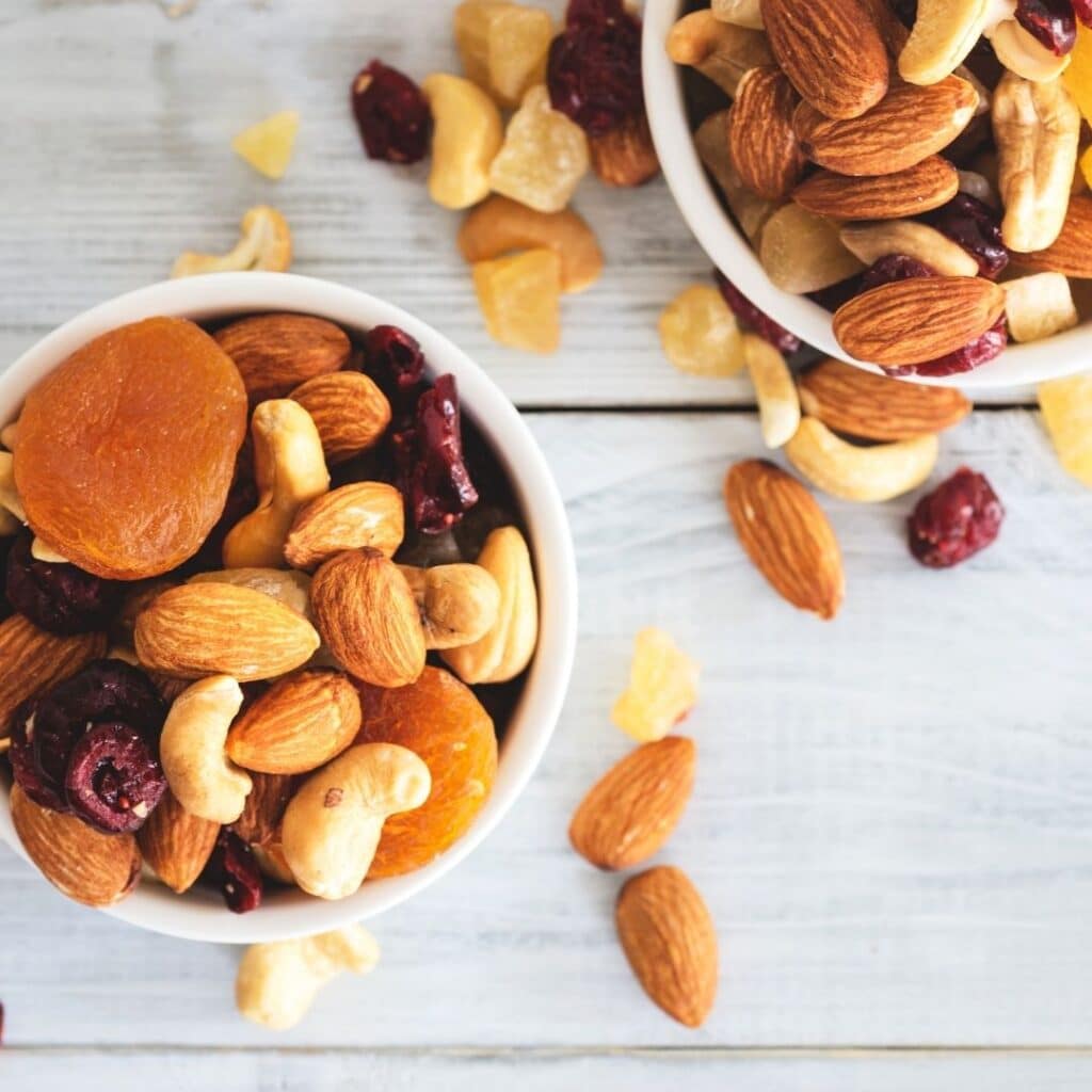 Trockenobst und Nüsse sind in 2 weißen Schüsseln angerichtet.
