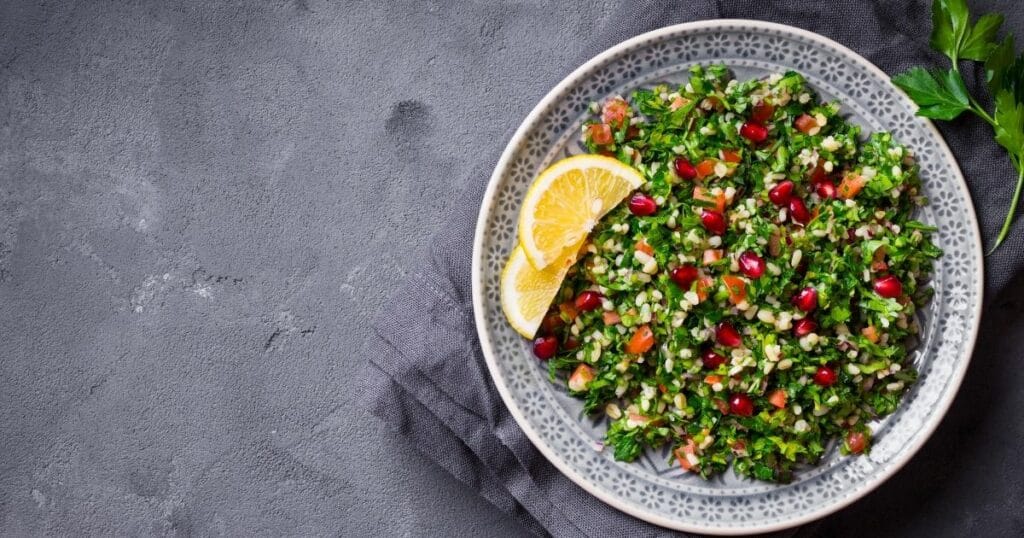 Eine Schale mit Bulgursalat und Zitronenscheiben steht auf grauen Servietten.