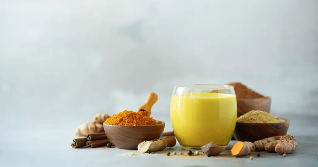 Ein Glas mit goldener Milch, daneben die Zutaten.