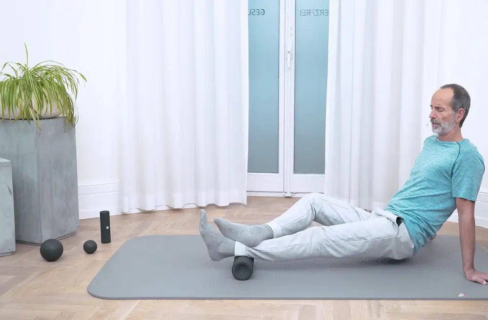Ein Mann liegt auf einer grauen Übungsmatte und führt eine Faszien-Rollmassage an der Wade durch