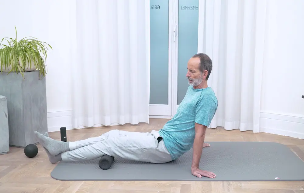 Ein Mann führt eine Faszien-Rollmassage an der Wade auf einer grauen Übungsmatte durch.