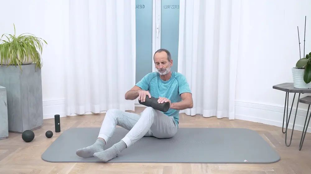 Ein Mann führt eine Faszien-Rollmassage an der Vorderseite des Beins durch und rollt dafür über die Kniescheibe