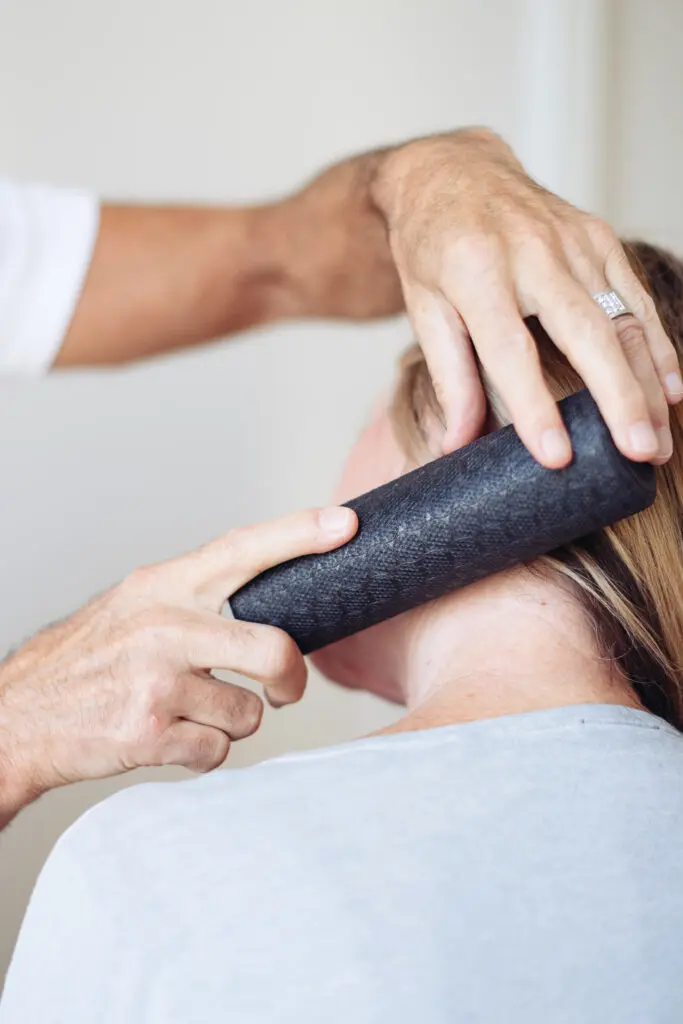 Eine Frau lässt sich zeigen, wie man die Nackenpartie mit der Mini-Faszienrolle ausrollt.