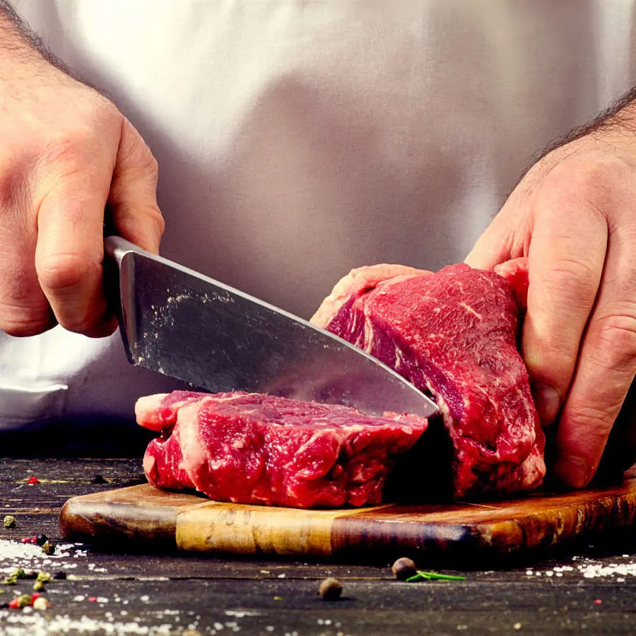 Ein Mann bereitet Fleisch zu, indem er Scheiben mit einem Metzgermesser von einem großen Fleischstück abschneidet.