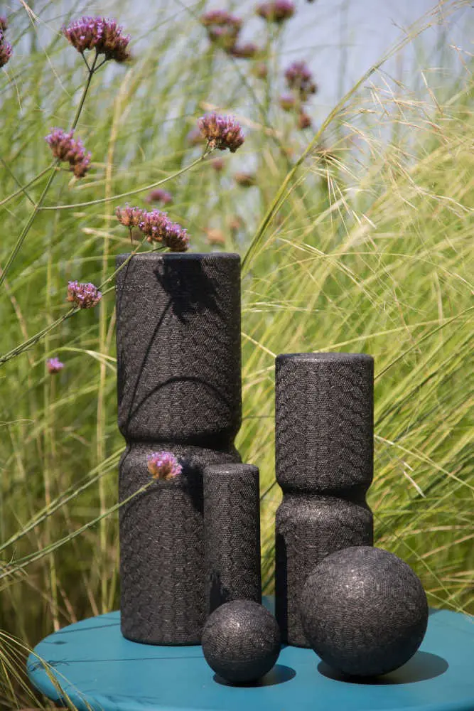 Zu sehen sind drei Faszienrollen und zwei Faszienkugeln, die auf einem Tisch vor einer Blumenwiese stehen