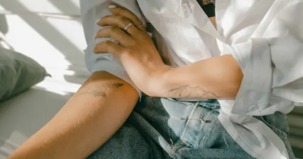 Eine Frau hat ihren Arm auf ihrem Oberschenkel abgelegt. Mit der anderen Hand greift sie den Oberarm.