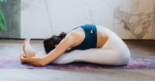 Eine Frau macht eine Dehnübung auf einer Matte, sie hat die Beine ausgestreckt und lehnt mit dem Oberkörper darüber.