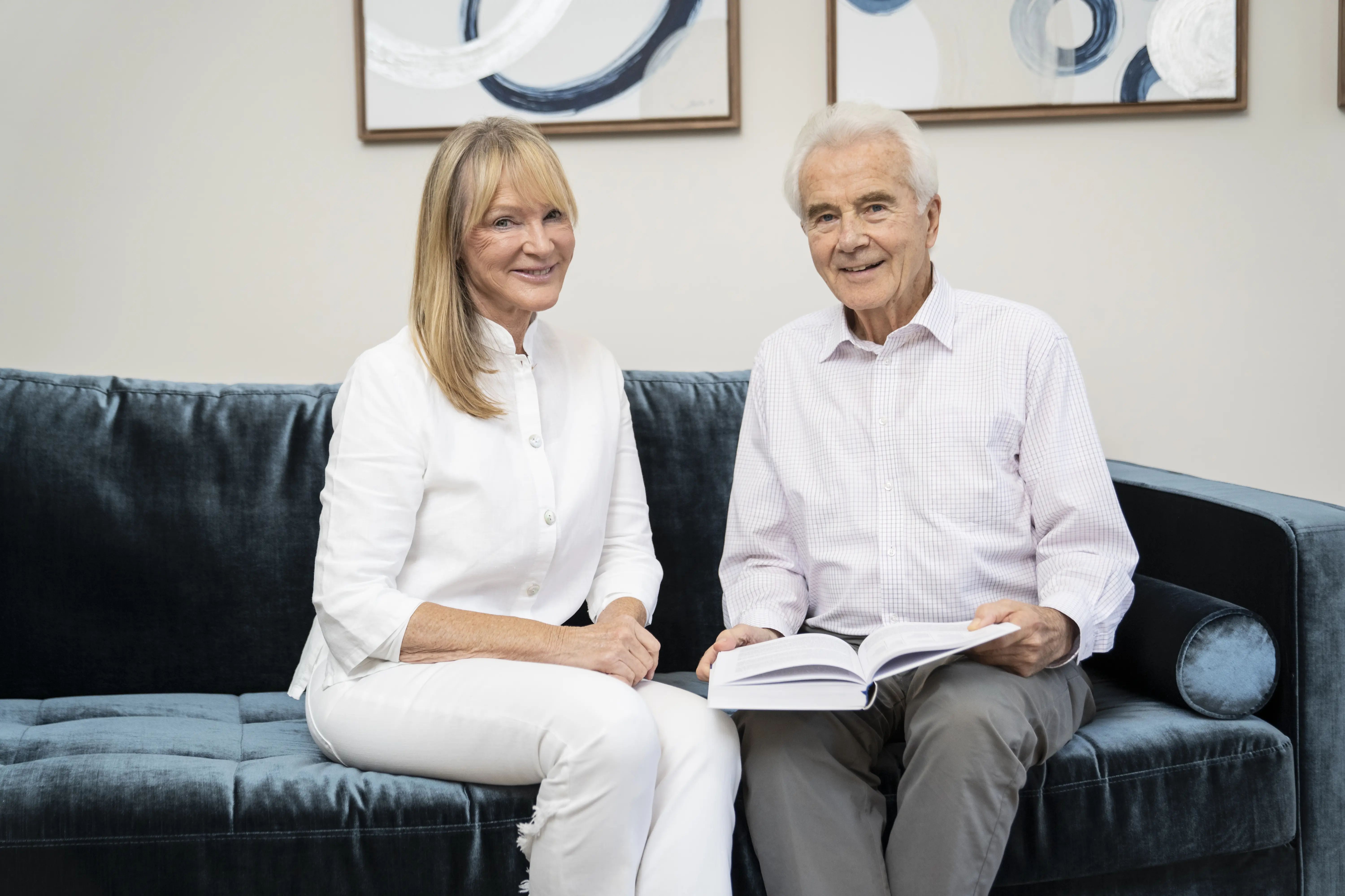 Dr. Petra Bracht und Prof. Dr. Claus Leitzmann sitzen zusammen auf einem dunklen Sofa und lächeln in die Kamera.