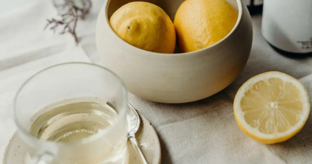 In einer Schale liegen Zitronen, daneben eine Tasse mit Tee und eine aufgeschnittene Zitrone