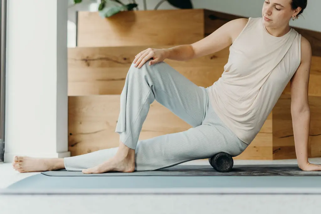 Eine Frau sitzt seitlich auf einer Maxi-Faszienrolle. Dabei ist ein Bein ausgestreckt, das andere angewinkelt.
