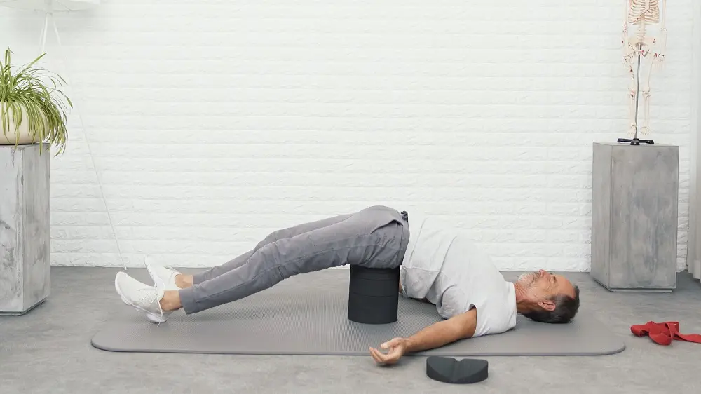 Ein Mann mit weißem Shirt und grauer Sporthose liegt auf dem Rückenretter von Liebscher & Bracht