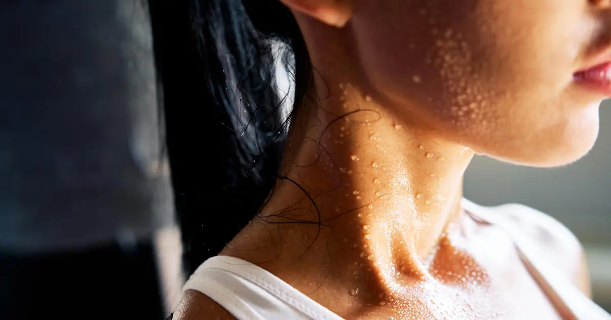 Eine junge Frau ist im Profil abgebildet. An ihrem Gesicht und Oberkörper sind Schweißperlen zu sehen.