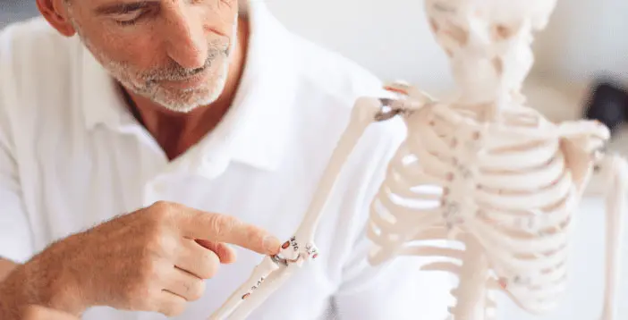 Roland Liebscher-Bracht zeigt auf einen rot markierten Punkt am Ellenbogen eines Skeletts.