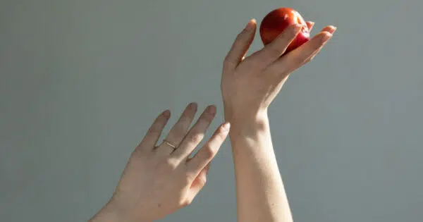 Arme einer Frau ragen in die Luft. Die rechte Hand hält einen roten Apfel