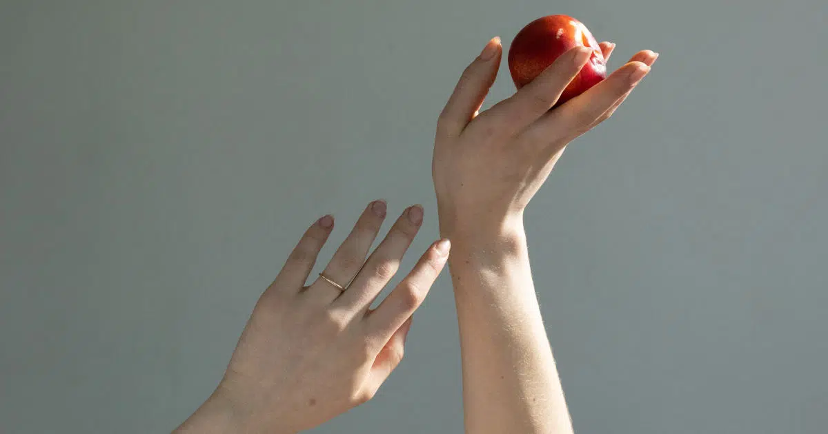 Arme einer Frau ragen in die Luft. Die rechte Hand hält einen roten Apfel