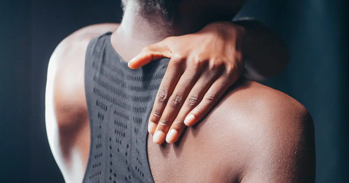 Eine Frau fasst sich mit der linken Hand an die rechte Nackenseite. Sie trägt einen schwarzen Sport-BH und hat schwarze Haare.