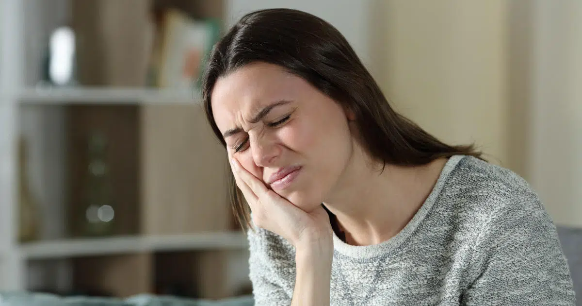 Eine junge Frau hält sich mit von CMD-Schmerzen erfülltem Gesicht ihren Unterkiefer.