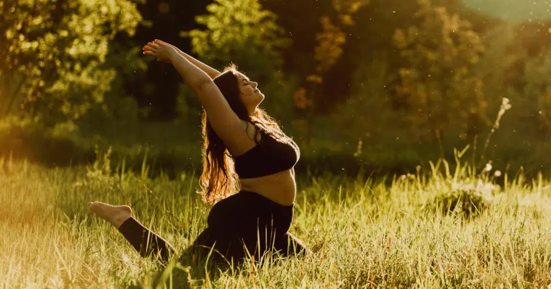 Eine Frau mit Übergewicht kniet auf einer Wiese und macht Übungen für mehr Beweglichkeit.