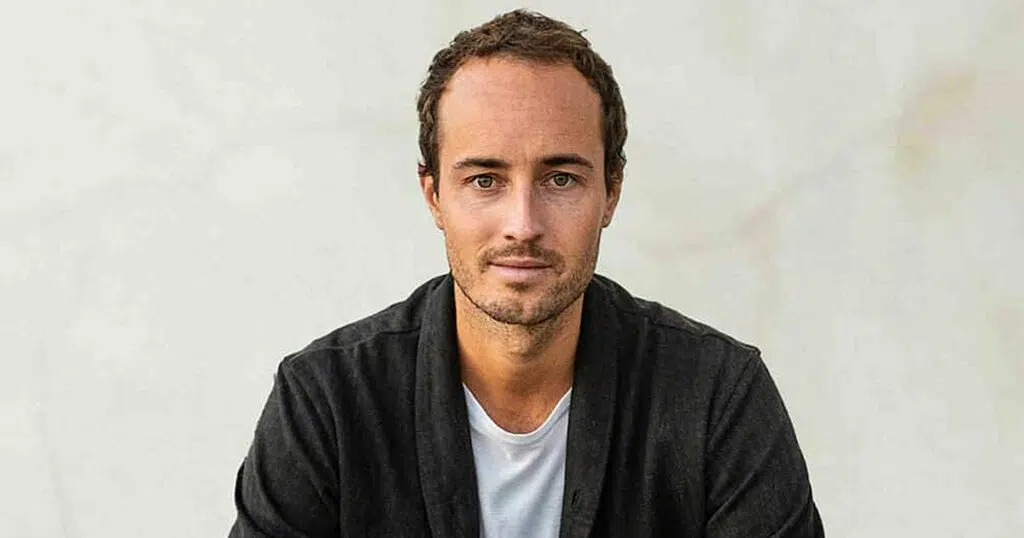 Zu sehen ist Raoul Bracht, der ein weißes T-Shirt mit einer schwarzen Jacke trägt und mit entschlossenem Blick leicht lächelnd in die Kamera schaut