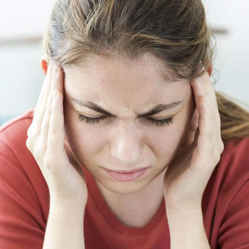 Eine junge Frau hält sich mit beiden Händen die Schläfen und schaut schmerzverzerrt