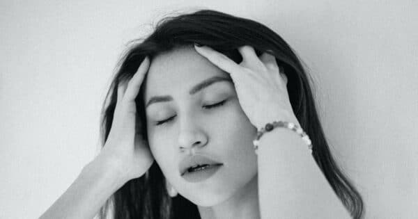 Eine junge Frau hält sich mit beiden Händen den Kopf