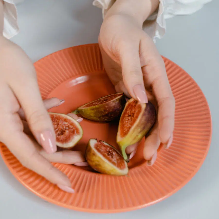 Auf einem orangefarbenen Teller liegen zwei halbierte Feigen, die eine Frau mit ihren Händen gerade anrichtet.