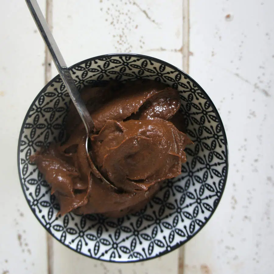 Eine Schüssel mit selbstgemachtem Schokoaufstrich steht auf einem Tisch. Ein Löffel liegt darin.