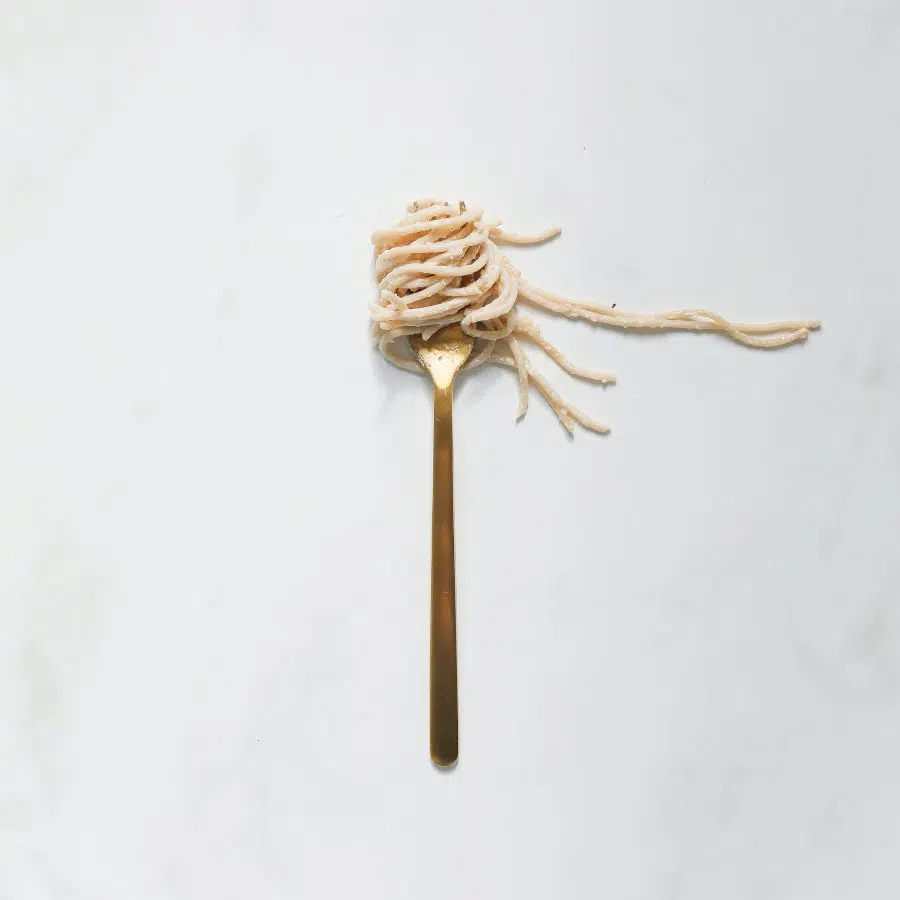 Eine Gabel mit aufgedrehten Spaghetti liegt auf einem weißen Untergrund