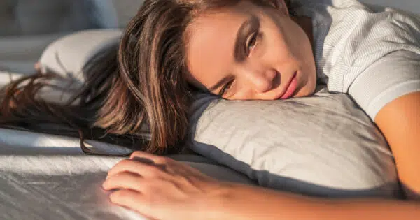 Frau liegt auf Bett und schaut müde und gestresst