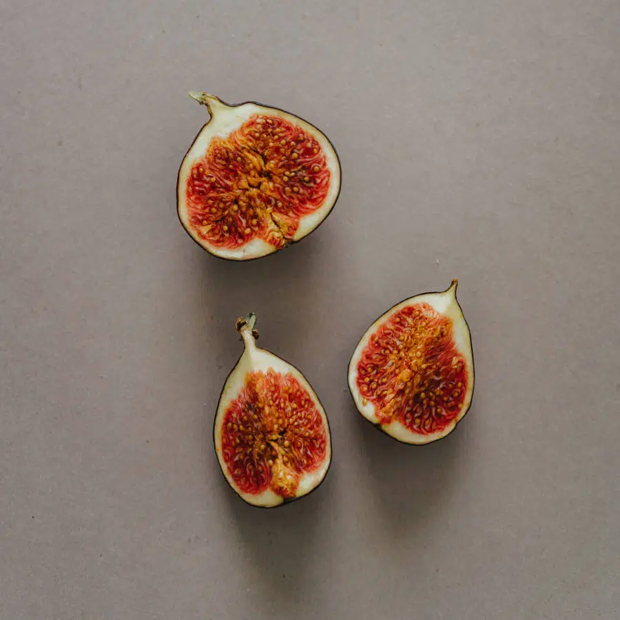 Eine Feige ist in drei Teile geschnitten. Zwei Viertel und eine halbe liegen auf einem beigen Hintergrund