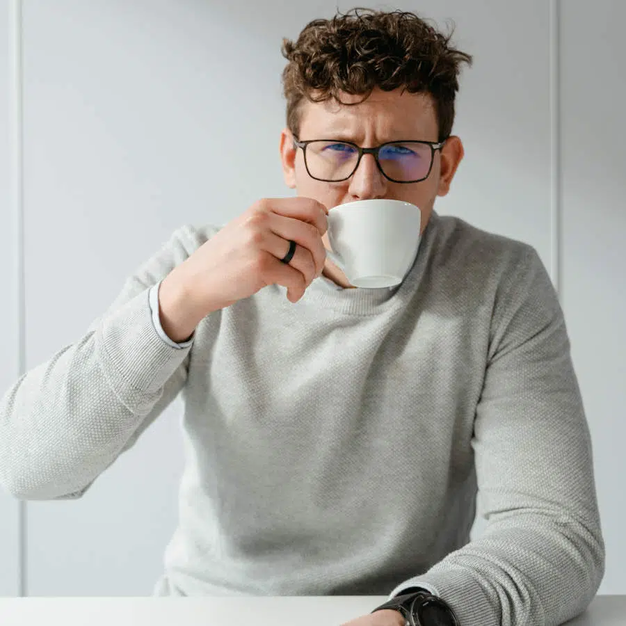Ein junger Mann trinkt eine Tasse Kaffee und schaut dabei sehr schlecht gelaunt aus.