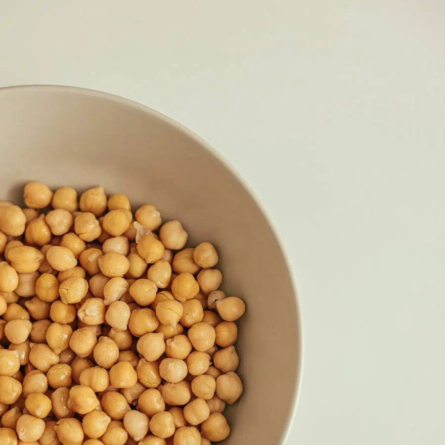 Jede Menge Kichererbsen sind in einer beigen Schale. Diese steht auf einem hellen Tisch.