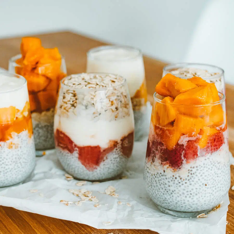 Fünf Gläser sind mit Joghurt, Chiasamen, Haferflocken und verschiedenem, geschnittenem Obst gefüllt.