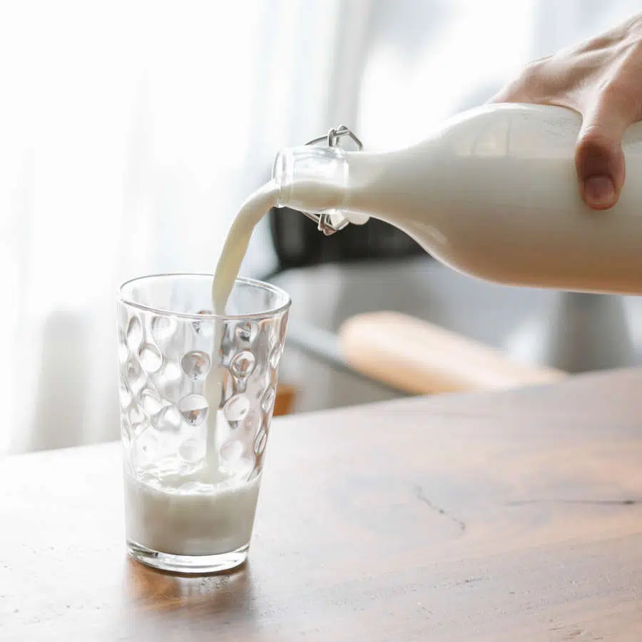 Eine Hand hält eine Glasflasche voll Kuhmilch und befüllt ein Glas mit Milch.