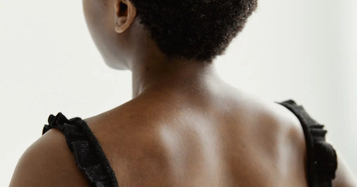 Eine Person ist von hinten zu sehen. Ihr Nacken, ihre Schultern und ein Teil des Kopfes sind abgebildet. Sie hat schwarze Haare und trägt ein schwarzes Oberteil.