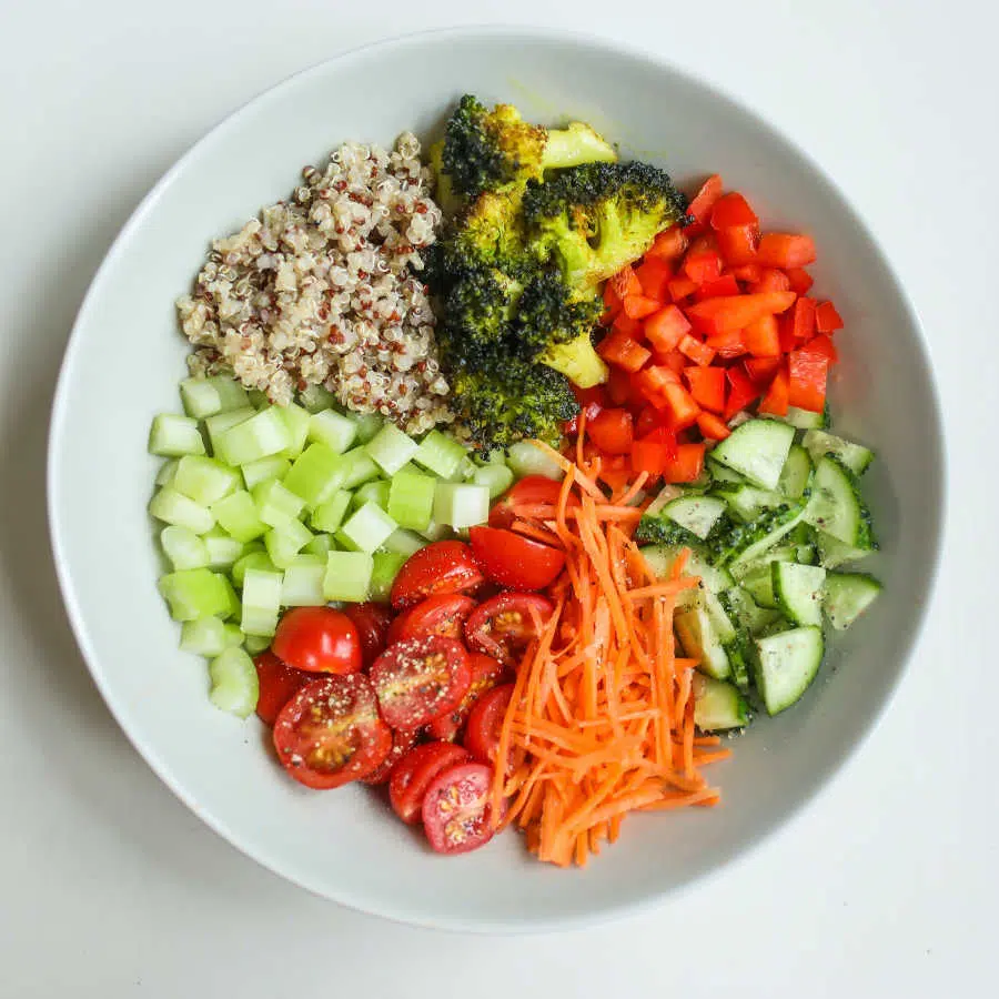 Ein Teller mit verschiedenem Gemüse und Quiona steht auf einem Tisch.