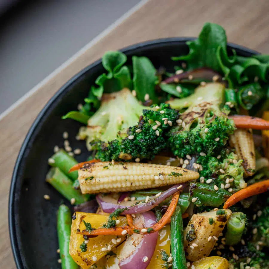 Eine Schüssel mit Salat und buntem gedünstetem Gemüse steht auf einem Tisch