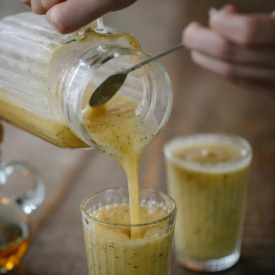 Eine Person füllt einen gelben Smoothie mit Chiasamen in zwei Gläser.