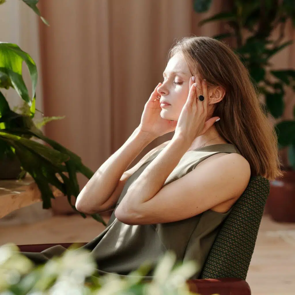 Eine Frau sitzt am Schreibtisch und massiert sich die Schläfen. Ihre Augen hälts sie dabei geschlossen.