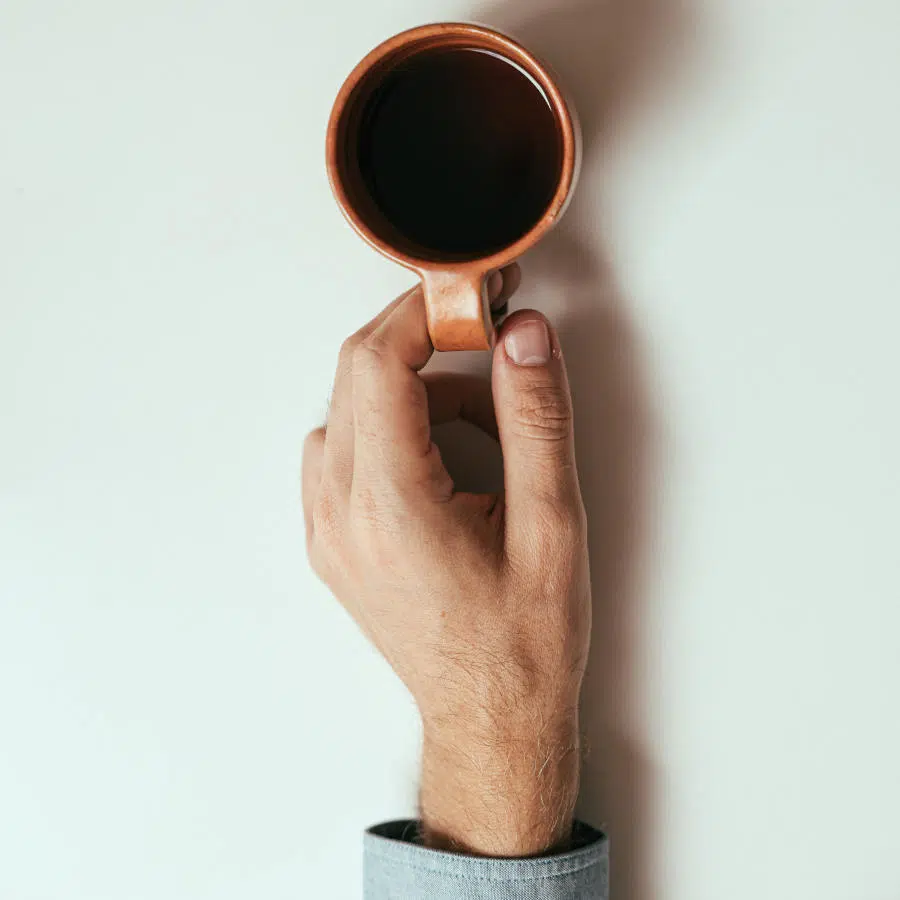 Im Bild ist eine männliche Hand, die eine Tasse entkoffeinierten Kaffee am Henkel festhält