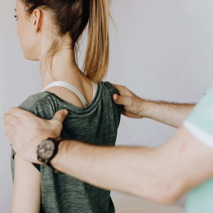 Eine junge Frau lässt sich am oberen Rücken und an den Schulterblättern von einem Arzt untersuchen