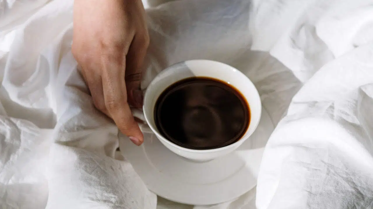 Eine Hand hält eine Tasse schwarzen Kaffee fest.